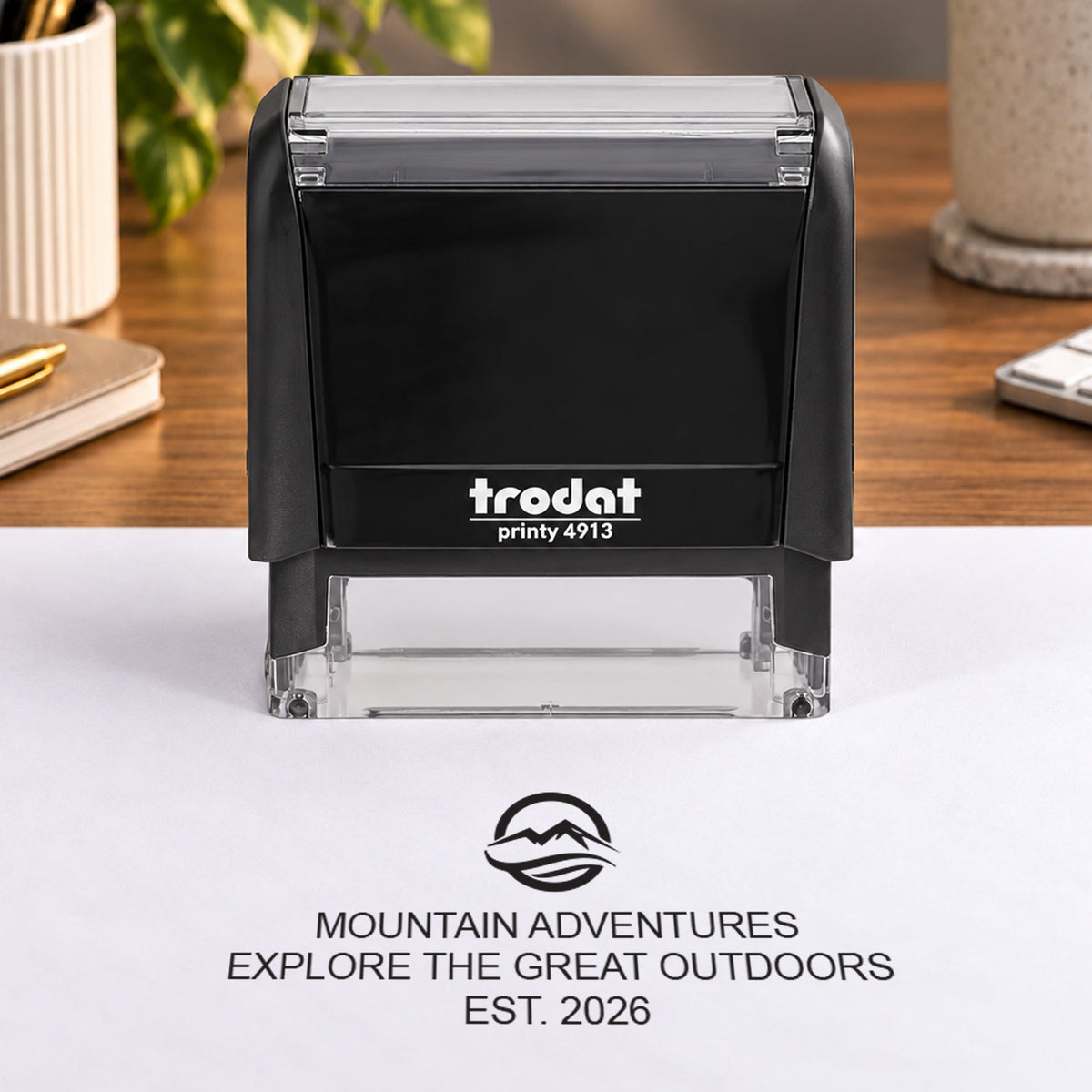 Trodat Printy 4913 on an office desk beside an example Mountain Adventures logo and wording in black