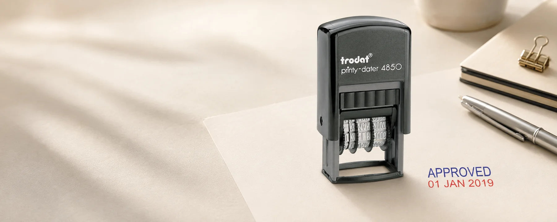 Trodat Printy-Dater 4850 beside its genuine blue and red approved date impression